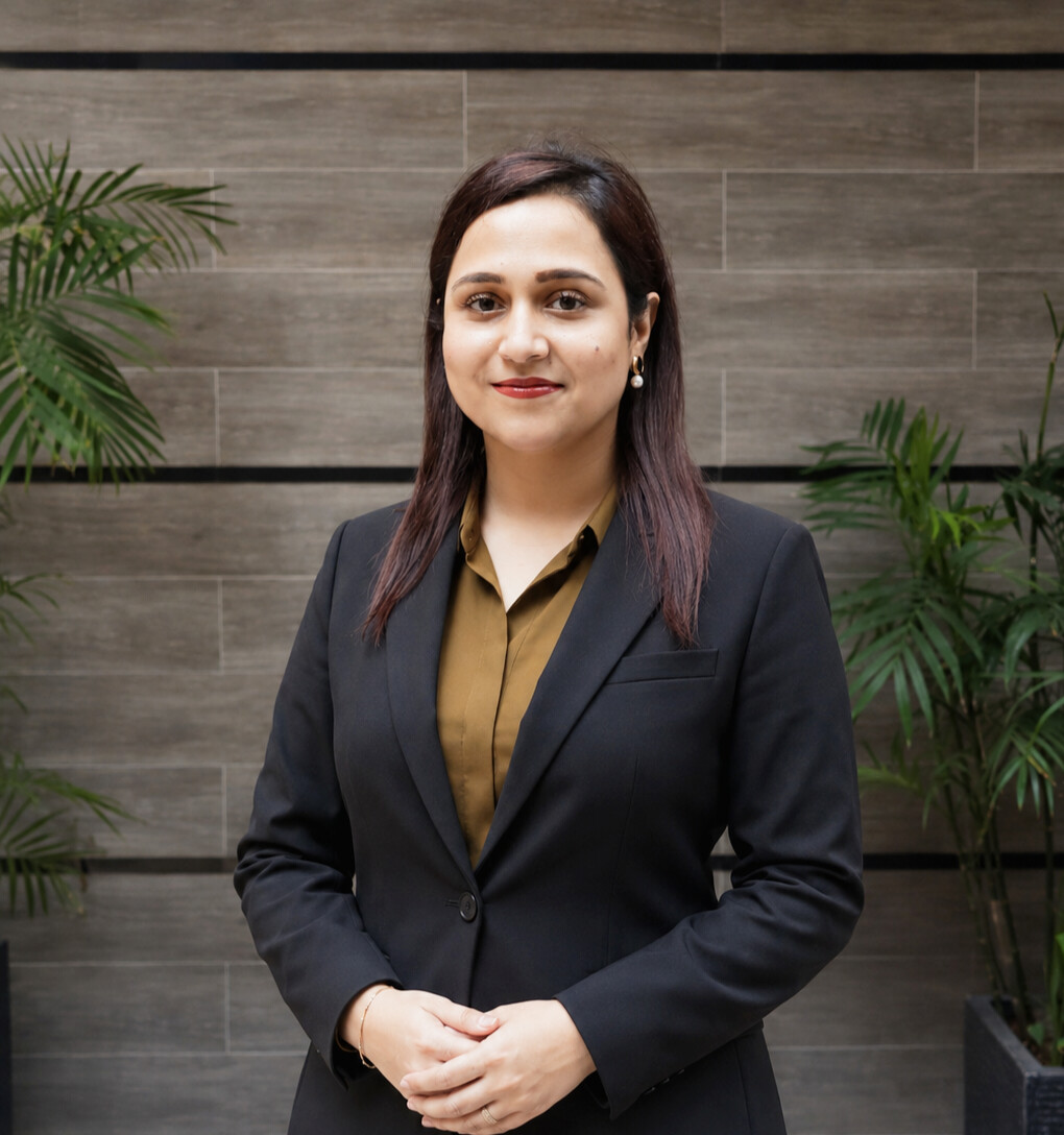 Portrait of Dr. Anum Ahad smiling, with long dark hair, wearing a black blazer over an olive blouse