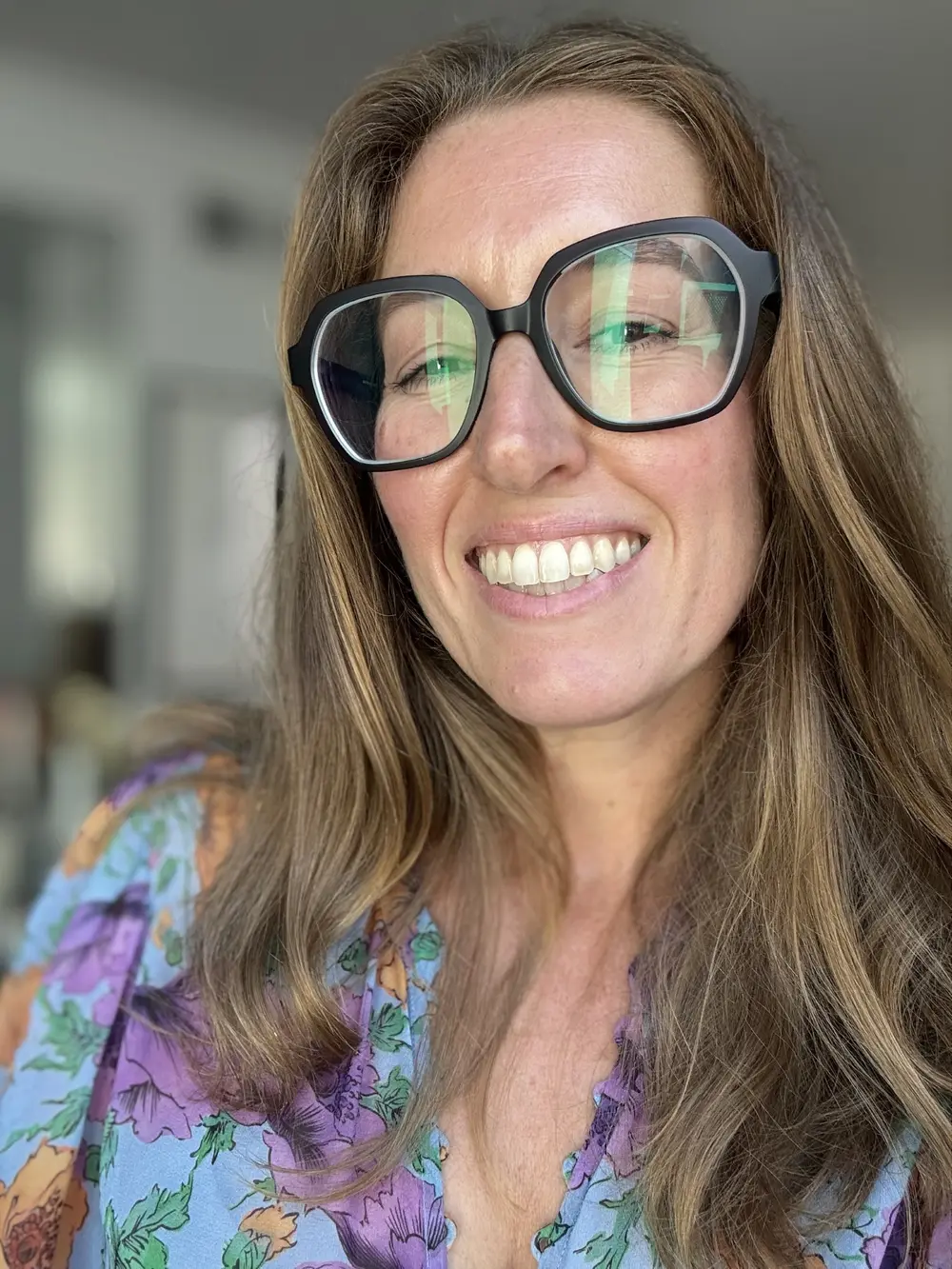 Portrait of Jenn Smukler smiling, wearing dark-framed glasses and a floral blouse
