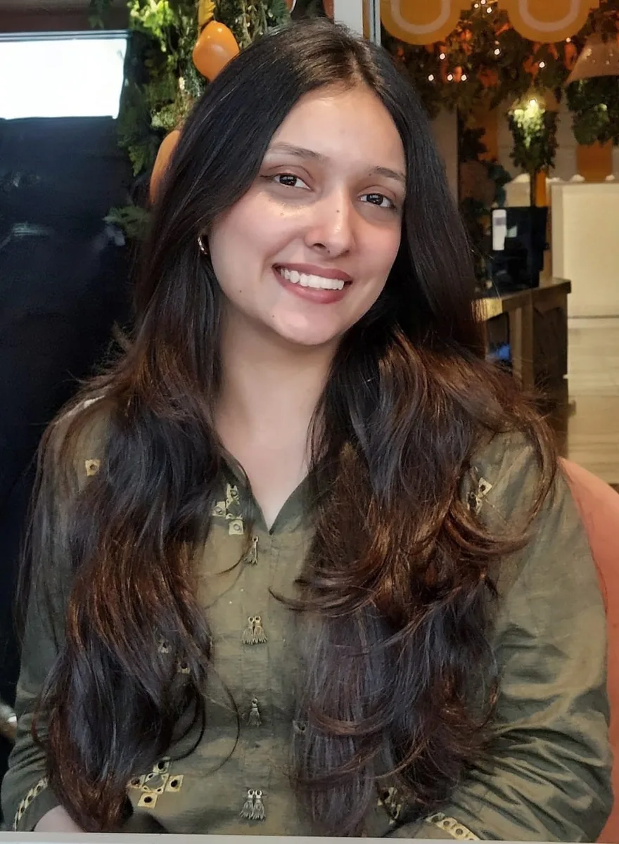 Portrait of Rabwa Sabeeh smiling, with long dark hair, wearing an olive embroidered top