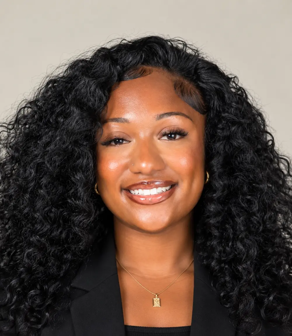 Portrait of Siani Brown smiling, wearing a black blazer and a gold pendant necklace